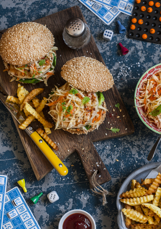 Hamburgers with grilled chicken and cole slaw on a wooden board on the table with cards and bingo chips, top view. Flat layの写真素材