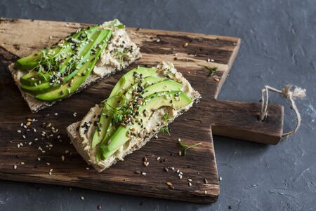 Miso tahini avocado sandwich on wooden cutting board on a dark background. Vegetarian snack