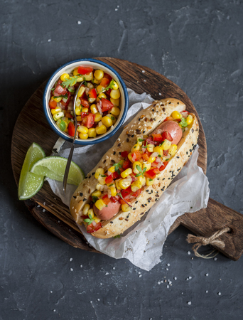 Mexican street style hot dog with corn salsa on a wooden cutting board on dark background, top viewの写真素材