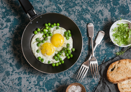 Delicious breakfast - fried eggs with green peas. On a dark background, top viewの写真素材