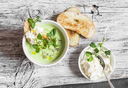 Green peas cream soup and cheese toast on the light wooden table, top viewの写真素材