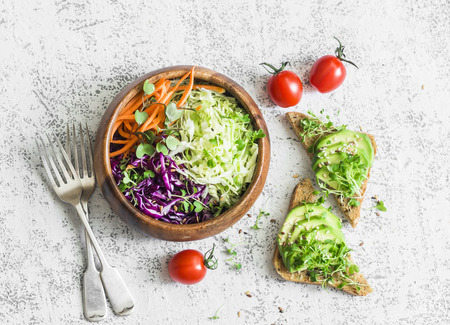 Spring healthy vegetarian snack - cabbage salad and sandwiches with avocado and micro greens on a light table, top view.の写真素材