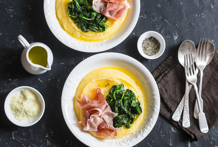 Polenta with butter spinach and prosciutto. Delicious lunch in a mediterranean style. On a dark background, top view. Flat layの写真素材