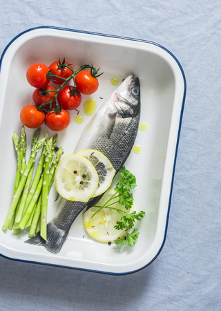 Raw sea bass, cherry tomatoes and asparagus in the baking tray. Ingredients for lunch. On a blue background, top viewの写真素材