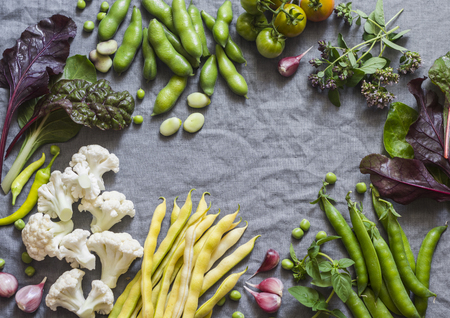 Food background. Fresh garden vegetables on grey background, top view. Cauliflower, beans, peas, chard, fava beans - organic veggies. Flat layの写真素材