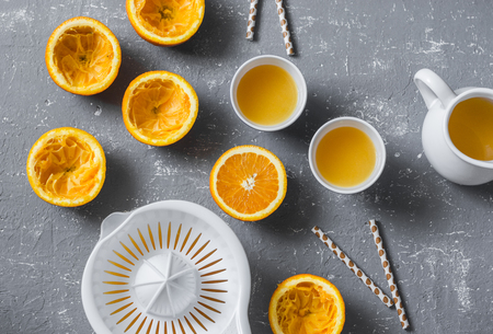 Cut oranges, fresh orange juice, manual citrus juicer on a grey table, top view. Healthy food conceptの写真素材