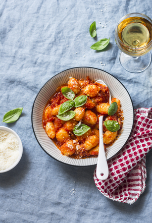 Potato gnocchi in tomato sauce with basil and parmesan and a glass of white wine on blue background, top view. Italian cuisine. Vegetarian foodの写真素材