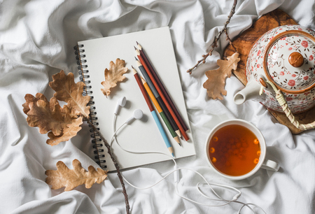 Drawing notepad, colored pencils, sea buckthorn tea, dried leaves of oak in bed, top view. Weekend cozy leisure concept. Flat lay. Autumn still lifeの写真素材