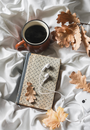 Coffee, book, headphones, phone on the bed, top view. Leisure, cozy home concept. Warm autumn moodの写真素材