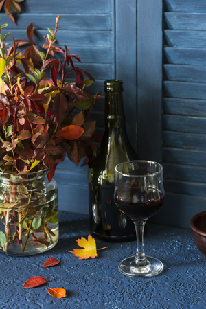 Autumn mood still life with a bouquet of autumn leaves and a glass of red wine on a wooden blue backgroundの写真素材