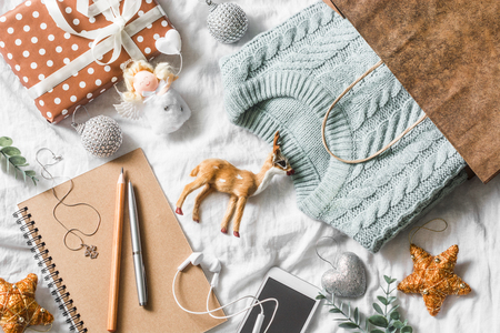 Christmas planning and shopping background. Blue knitted sweater in a paper bag, notepad, phone, christmas decoration on a light background, top view. Christmas still lifeの写真素材