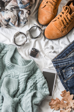 Flat lay women's clothing for autumn walks, top view. Brown suede boots, jeans, a blue pullover, scarf, bracelets, watches, headphones, perfume on a light background. Fashion conceptの写真素材
