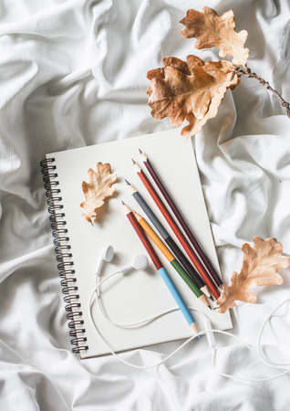 Drawing notepad, colored pencils, dried leaves of oak, headphones in bed, top view. Weekend cozy leisure concept. Flat lay. Autumn still lifeの写真素材