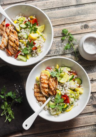 Pearl barley with seasonal garden vegetables and grilled chicken on wooden background, top view. Healthy balanced food conceptの写真素材