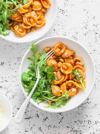 Pasta with beans, tomato sauce, parmesan and arugula on light background, top view. Vegetarian beans orecchiette pastaの写真素材