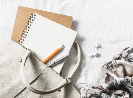 Womens leather handbag, clean blank notepad, pen and scarf on a light background, top view. Free...