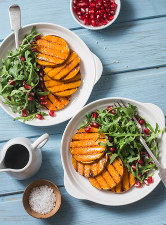 Grilled butternut squash, arugula and pomegranate salad on a blue wooden table, top view. Clean, organic, seasonal, vegetarian food conceptの写真素材
