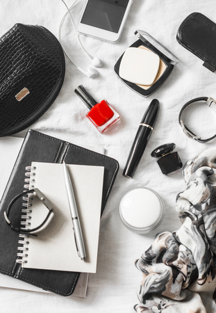 Woman beauty accessories on a light background, top view. Cosmetic bag, red nail polish, mascara, watch, bracelet, scarf, perfume, powder, phone, headphones, notepad - flat lay still lifeの写真素材