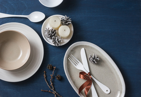 Christmas lunch food served table. Empty plates, bowls, fork, knife, spoon, christmas decorations, cones and candles on blue wooden background, top view. Flat lay, free spaceの写真素材