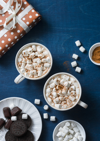 Christmas inspiration table - hot chocolate with marshmallows, cookies, gift box, christmas ornament reindeer on a blue background, top view. Flat layの写真素材
