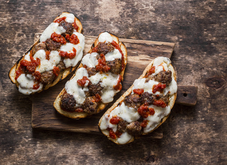 Meatballs, tomato sauce, mozzarella and arugula hot sandwiches on a rustic cutting board on a wooden table, top view. Delicious snack, breakfast, appetizerの写真素材