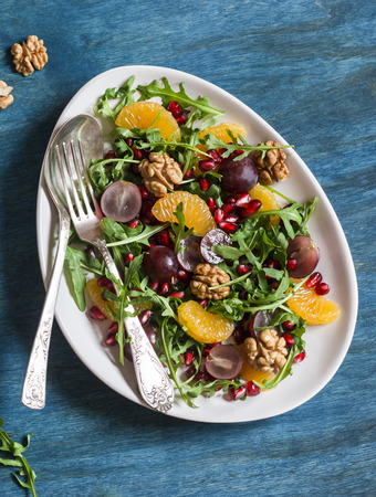 Salad with tangerines, grapes, arugula, pomegranate and walnuts with a honey dressing on a blue background, top viewの写真素材