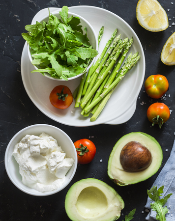 Healthy food ingredients - avocado, asparagus, tomatoes, sheep cheese, arugula on dark background, top view. Healthy clean eating conceptの写真素材
