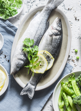 Fresh raw sea bass and vegetables on a light background, top view. Healthy food ingredientsの写真素材