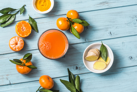 Carrots, ginger, tangerines, turmeric detox fresh juice on blue wooden background, top view. Healthy...