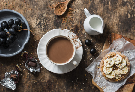 Cocoa, cracker with peanut butter, banana, flax  and chia seed, grapes - snack, breakfast table. Cosy atmosphere breakfast on wooden background, top viewの写真素材