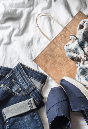 Women's clothing buy concept. Jeans, sneakers, scarf, paper bag on a light background, top viewの写真素材