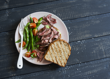 Green beans and grilled steak on toast. Steak sandwich and green beans - healthy snack on a dark background, top viewの写真素材