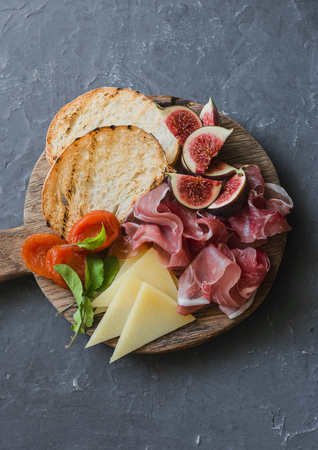 Delicious appetizers for wine or a snack - prosciutto, figs, bread, cheese on a rustic wooden cutting board. On a gray background, top viewの写真素材