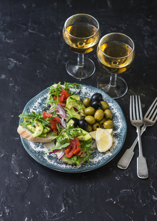 Mediterranean style antipasto and wine. Smoked salmon, avocado, arugula bruschetta, olives and two glasses of white wine on dark backgroundの写真素材