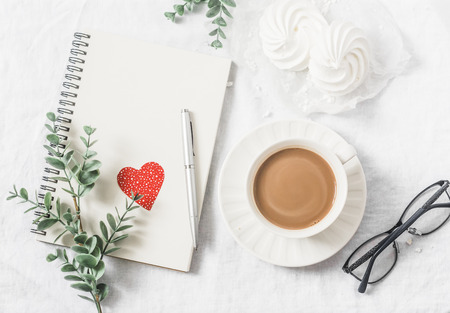 Flat lay Valentine's day breakfast - cocoa with milk, meringues, flowers, notepad, paper hearts decorations, glasses on a light background, top view. Free space for textの写真素材