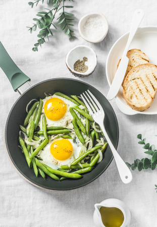 Healthy breakfast or snack - a fried egg with green beans in the pan on a light background, top viewの写真素材