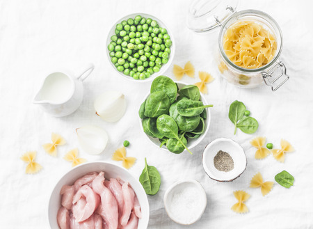 Ingredients for cooking one pot creamy chicken spinach and green peas farfalle pasta on white background, top view. Flat layの写真素材