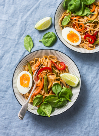 Yaki Udon noodles with stir fry vegetables, boiled egg and spinach. Vegetarian noodles with green beans, sweet peppers, mushrooms, carrots - healthy foods for lunch on a blue background, top viewの写真素材
