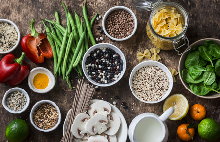 Flat lay vegetarian healthy food set - grains, vegetables, fruit, pasta, seeds on a brown wooden background, top view. Healthy food conceptの写真素材