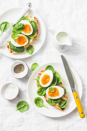 Served Easter brunch plate - grilled bread sandwich with spinach and boiled eggs on white background, top viewの写真素材