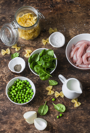 Ingredients for cooking one pot creamy chicken spinach and green peas farfalle pasta on wooden background, top view. Flat layの写真素材