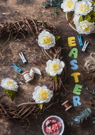 Flat lay handmade Easter decorations - wreath of vines with flowers, paper rabbits, ribbons on a wooden background, top view. Easter craft decorations home interior. Creativity conceptの写真素材