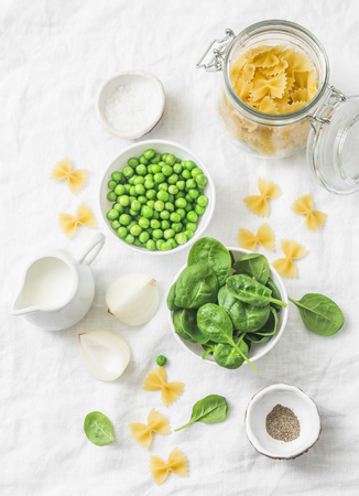 Healthy food ingredients for lunch - pasta farfalle, spinach, green peas, cream on white background, top viewの写真素材