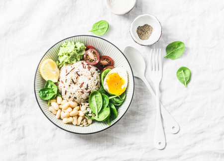 Wild rice, boiled egg, spinach, avocado puree, beans, tomatoes buddha bowl on light background, top view. Healthy vegetarian food conceptの写真素材