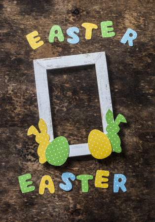 Flat lay Easter background. Empty frame, paper homemade rabbits on wooden rustic background, top view. Easter decorations. Free space for textの写真素材