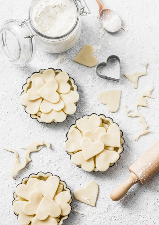 Flat lay Valentine's day baking background. Raw apple tartlets in the baking dish and baking ingredients on light background, top viewの写真素材