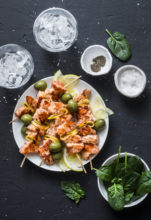 Salmon skewers, olives, spinach, ice water - snack table. Grilled salmon fish skewer on a dark background, top viewの写真素材