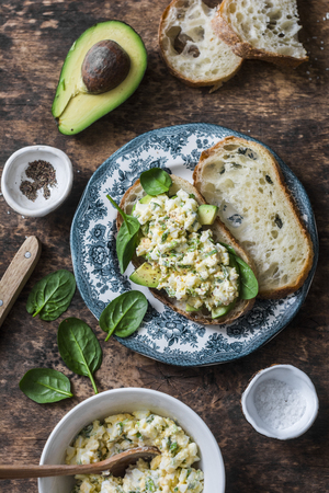 Avocado, spinach, egg salad on toast sandwich. Healthy food breakfast, snack on wooden background, top view. Flat layの写真素材