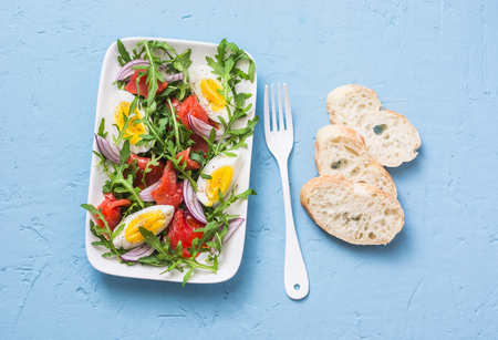 Smoked salmon, eggs, arugula, red onion, olive oil, lemon dressing salad on blue background, top view. Flat layの写真素材