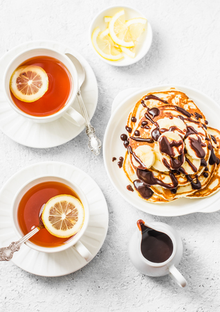 Coconut flour pancakes with banana and chocolate sauce and tea with lemon on a light background, top view. Delicious breakfast, dessert, snackの写真素材